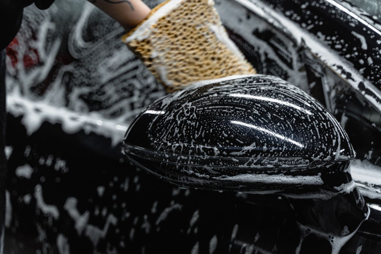 Home Hand scrubbing a car mirror with a sponge covered in soap at a car wash.
